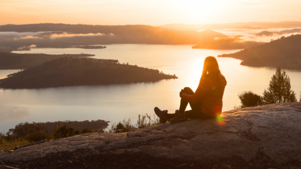 Femme sur le haut d'une montagne qui contemple lac au coucher du soleil